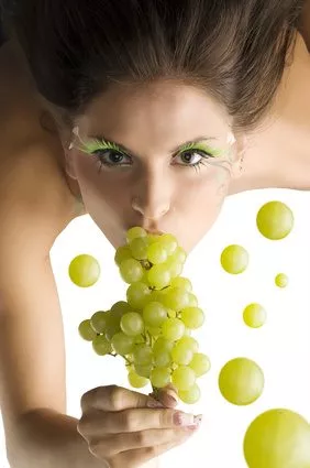 cute girl eating some green grape and looking in camera